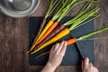 WomanÃ¢â¬â¢s hands cutting rainbow carrots on a black cutting board, stainless-steel bowl, wood table Royalty Free Stock Photo